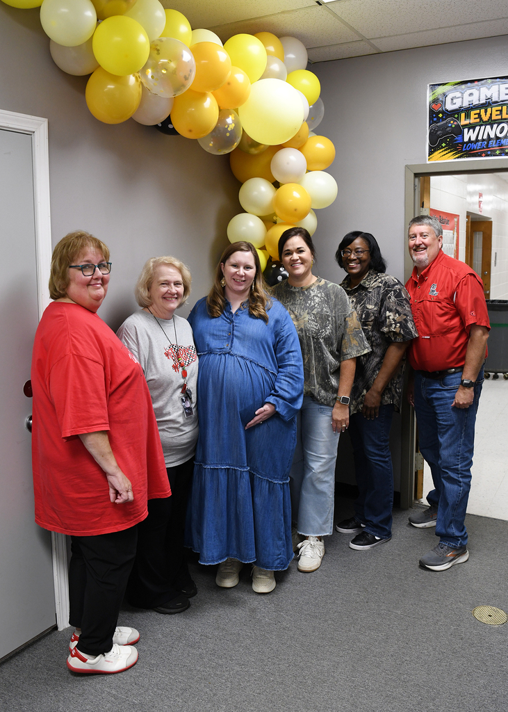Six people stand in front of a doorway with balloons. A sign behind them says Game Level Winner.