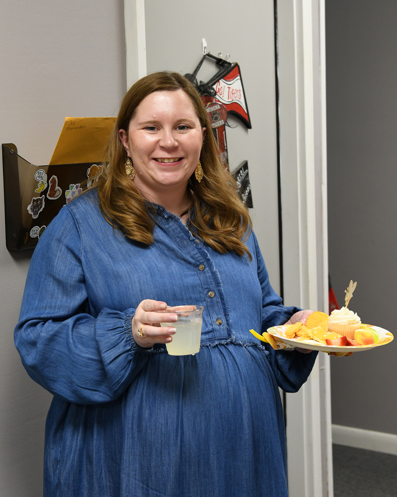 Person in blue dress holds a glass of juice and a plate of fruit in an office.