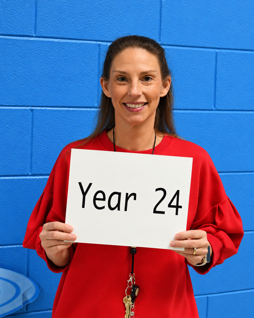 A woman in a red shirt holds a white sign reading "Year 24" in front of a blue background.