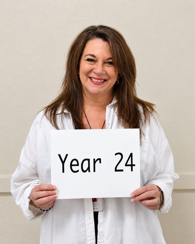 A woman wearing a white shirt holds a white sign that reads "Year 24" and smiles at the camera.