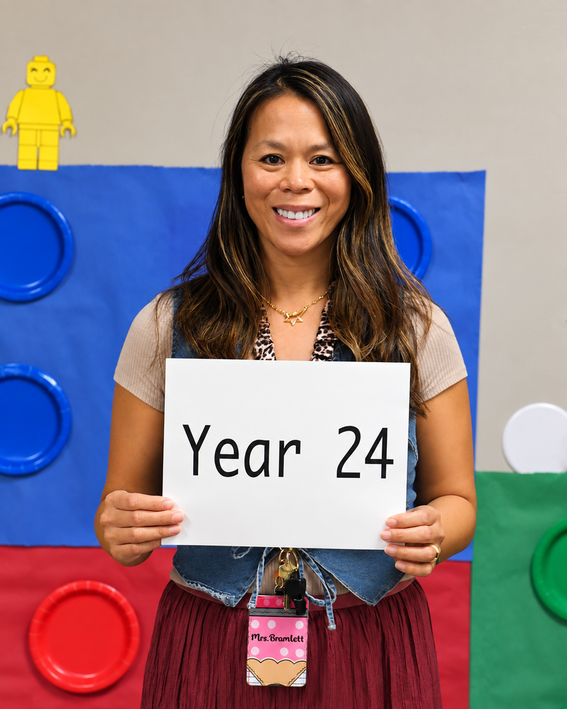 A woman in a denim vest and a red skirt holds a sign reading "Year 24" in front of her.