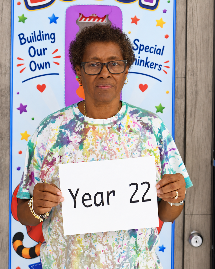 A person holds a white sign with the number 22. They wear a tie-dye shirt and stand in front of a colorful wall.