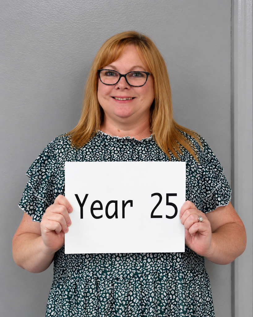 Woman wearing a blue dress holds a sign saying "Year 25" in front of a gray wall.