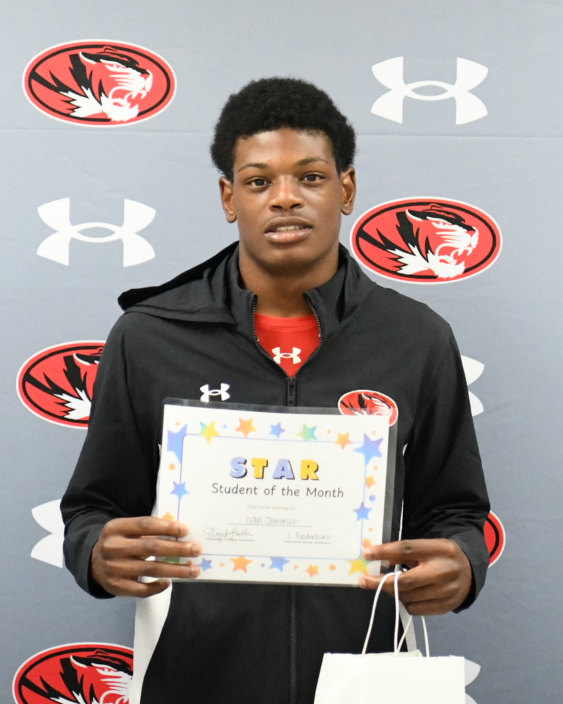 A man in a black jacket holds a "STAR Student of the Month" certificate. A white bag is in his hand.