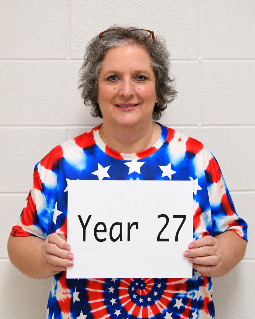 Person wearing a shirt with stars and stripes holds a white sign with black text that reads "Year 27."