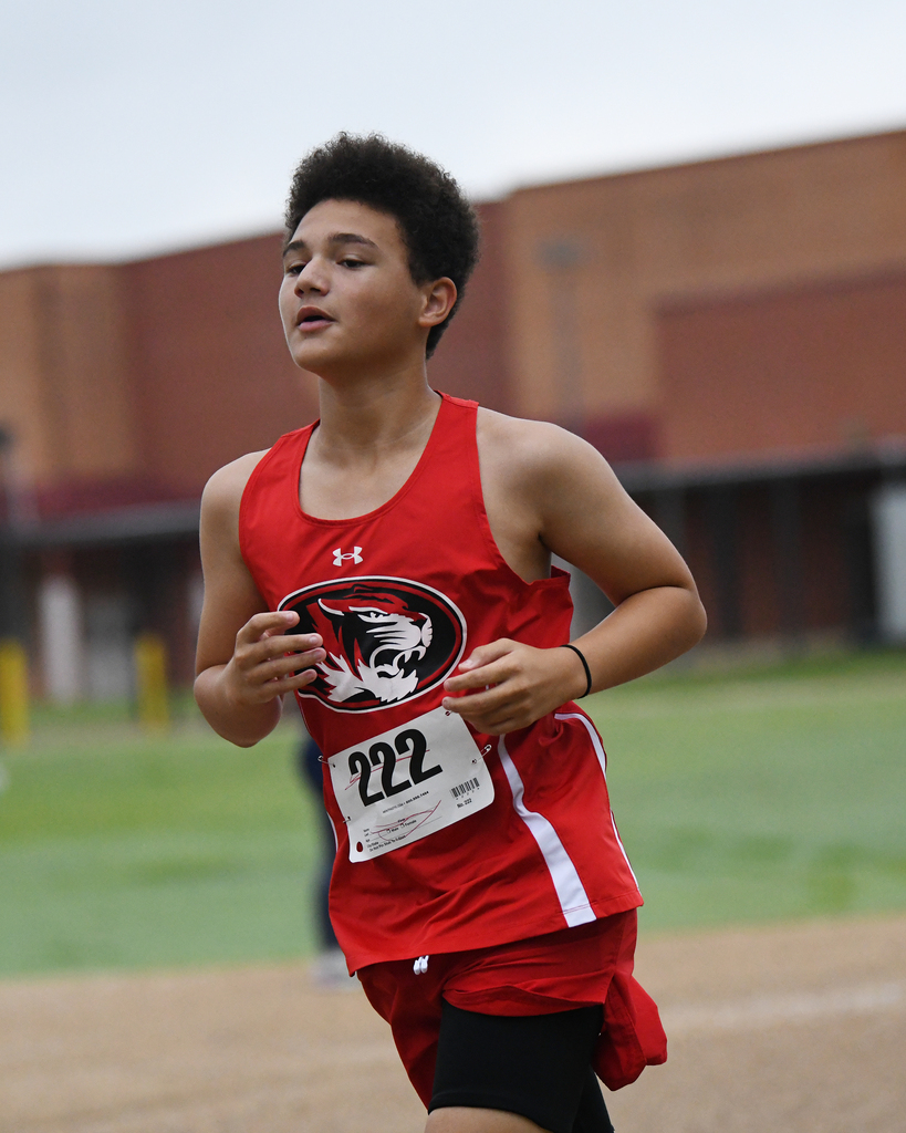 A boy with a red jersey and number 222 runs on a track, focusing on the ground.
