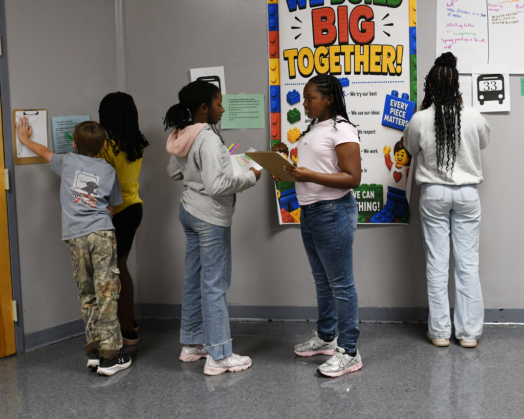 Group of five children standing in a classroom. One child writing on a board.