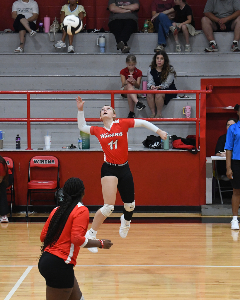 Volleyball player in red jersey jumping to hit ball. Another player in red jersey waiting to receive.