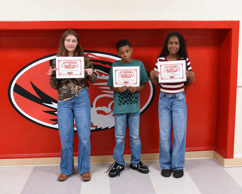 Three students hold certificates in front of a red wall with a black and white eagle logo.