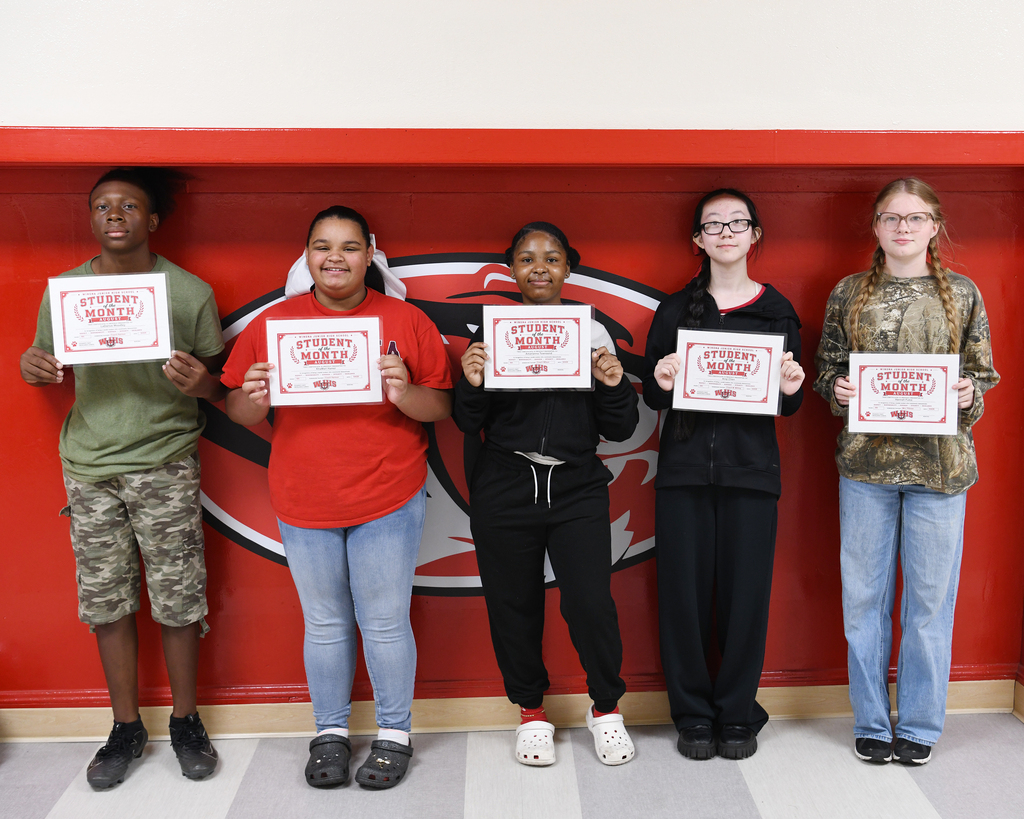 Five students hold certificates, standing in front of a red wall with a black and white logo.