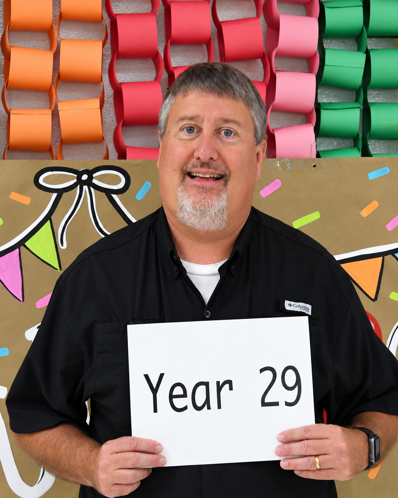 Man holds a white sign reading "Year 29" in front of colorful, decorative paper chains.