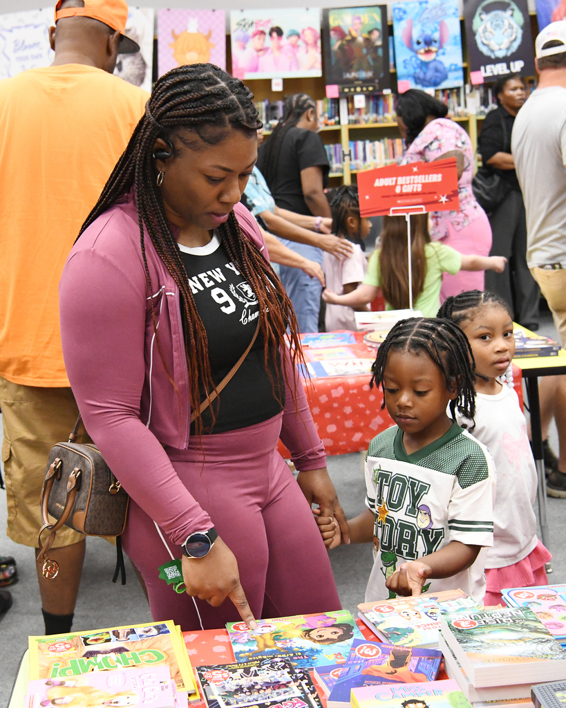 Woman with two children at a book stall, surrounded by people and shelves in the background.