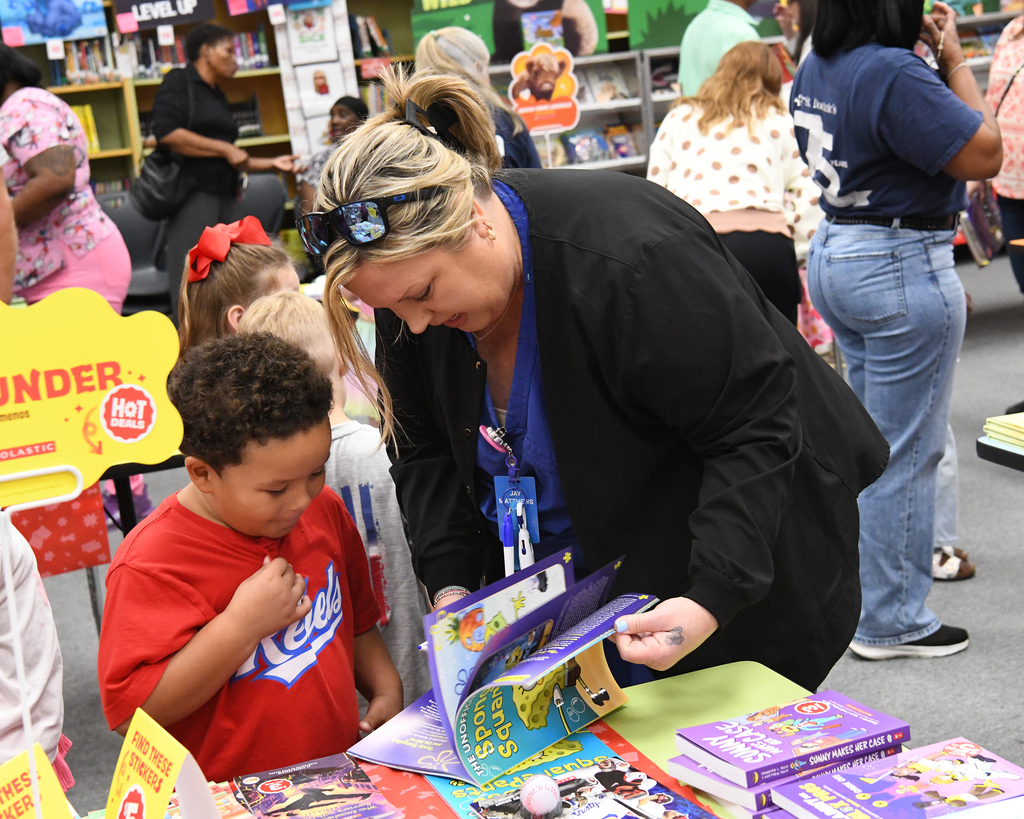 Woman assisting a child in selecting a book among a collection at a library event.