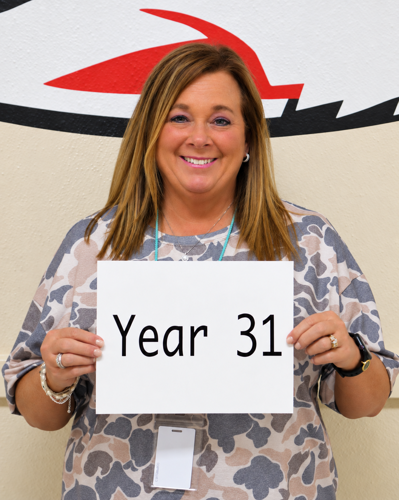 A woman in a patterned top holds a white sign saying "Year 31" with a shark logo in the background.