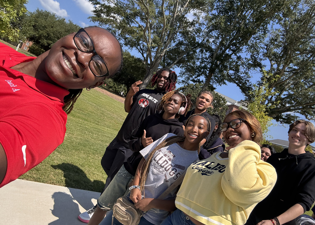 A group of individuals posing together outdoors. Two wear glasses, and three wear yellow and black.