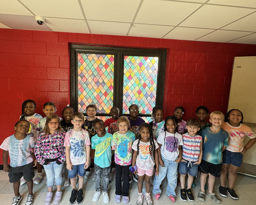 A classroom with red walls has a group of children wearing colorful shirts and sneakers posing for a photo.
