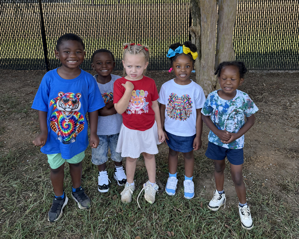 Five children, varying in height, standing outside. Two of them wear sneakers, one wears sandals, and two wear shoes.
