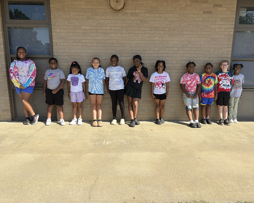 Group of children standing together in front of a brick building. They are wearing casual clothes and shoes.