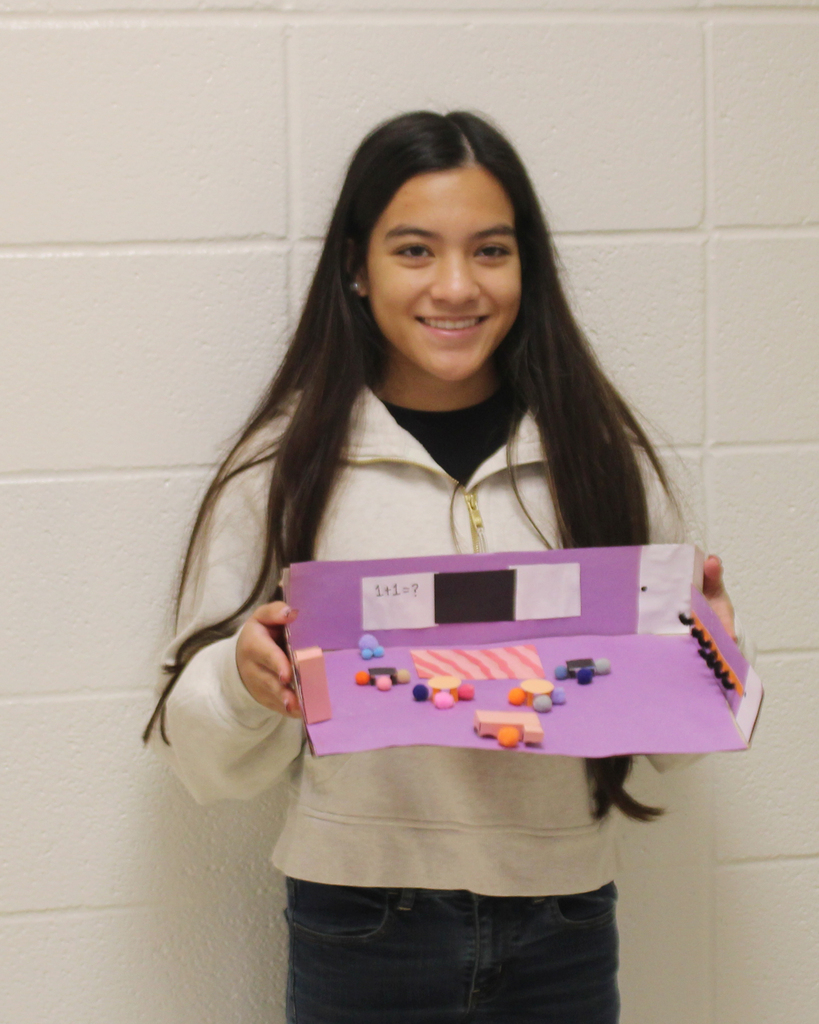 A person holds a colorful model in hand. The model resembles a candy store with sweets displayed on the countertop.