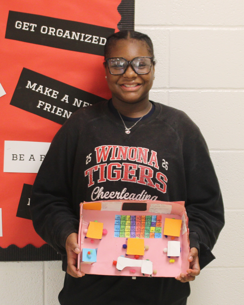 Woman wearing glasses and a Winona Tigers sweatshirt holding a pink box with a model on it.