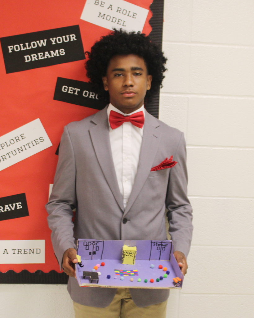 Person in suit stands in front of motivational poster. Holding a colorful game board.
