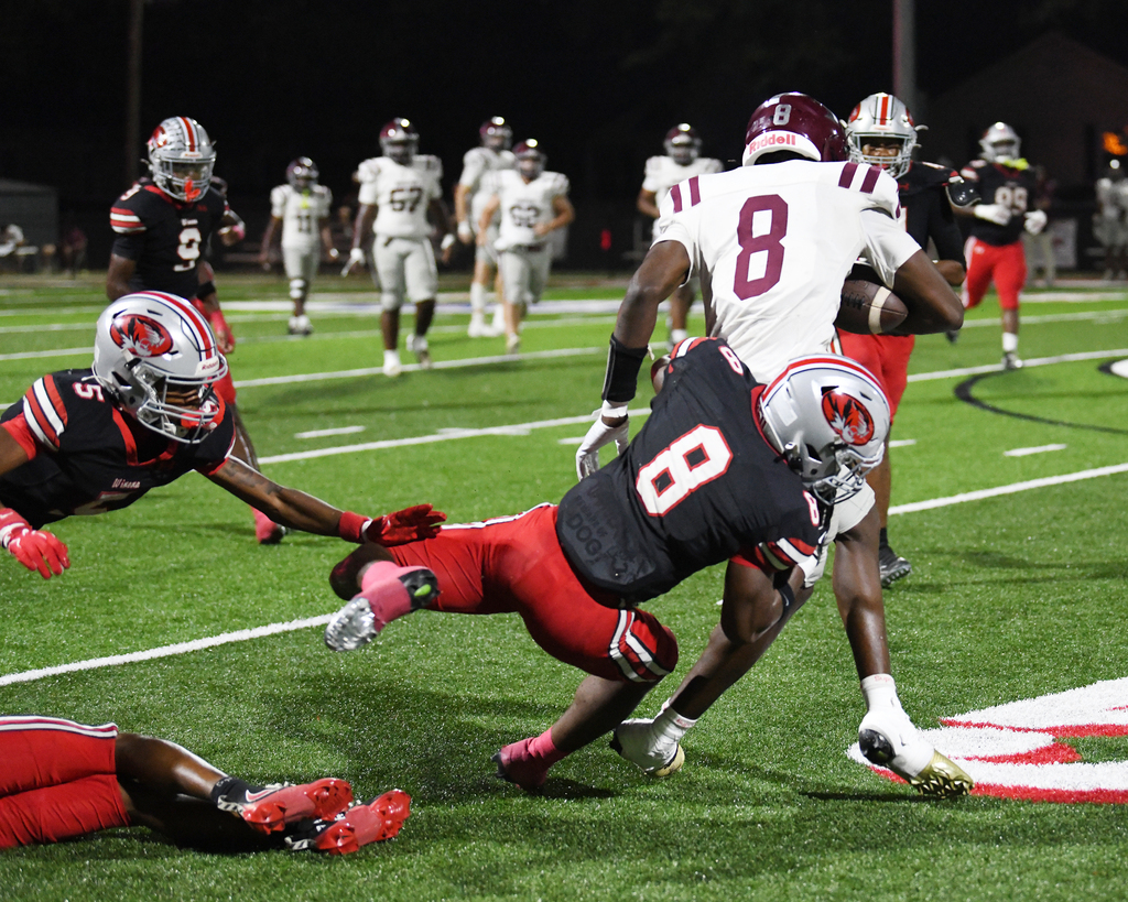 American football players in maroon and red uniforms on a field. Players with numbers 8 and 11 are tackling.
