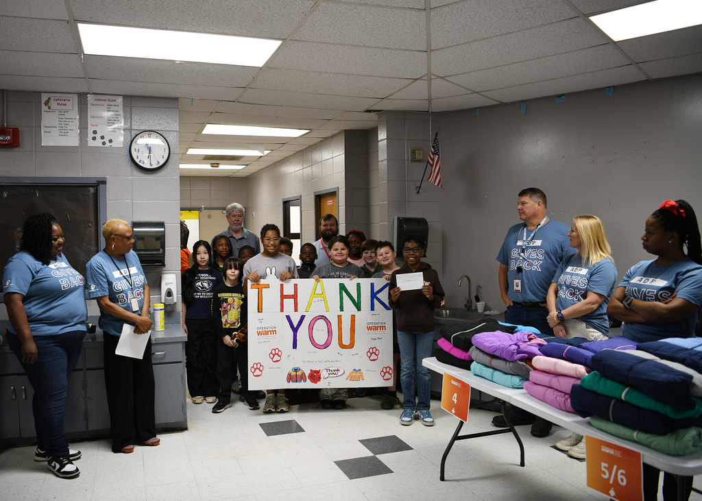 A group of people in blue shirts holding a sign that reads Thank You. Tables with folded clothes.