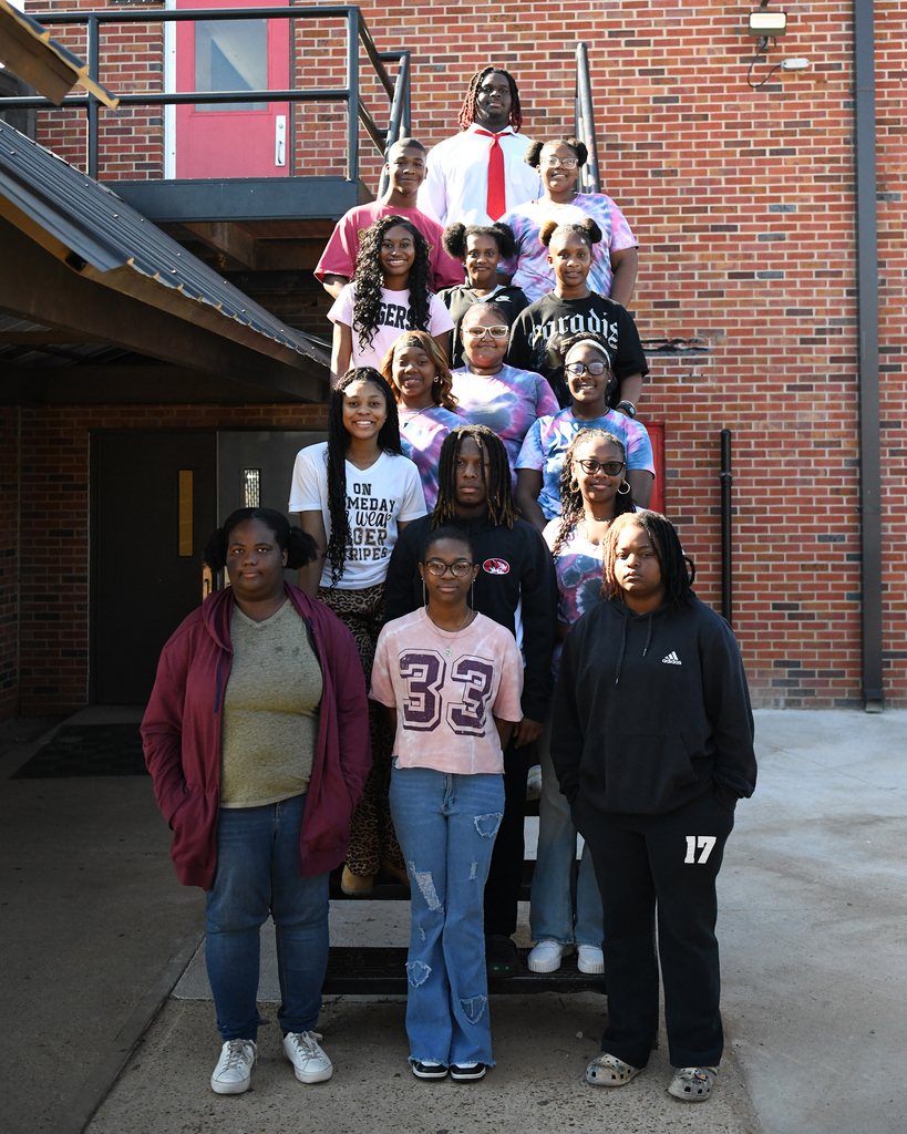 A group of women and girls pose outside a brick building with a red door, standing on steps.