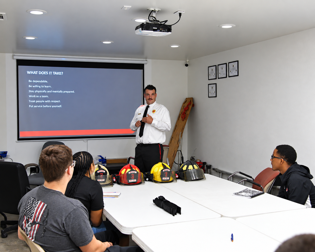 A classroom with a projector screen shows a person giving a presentation to a group of people.