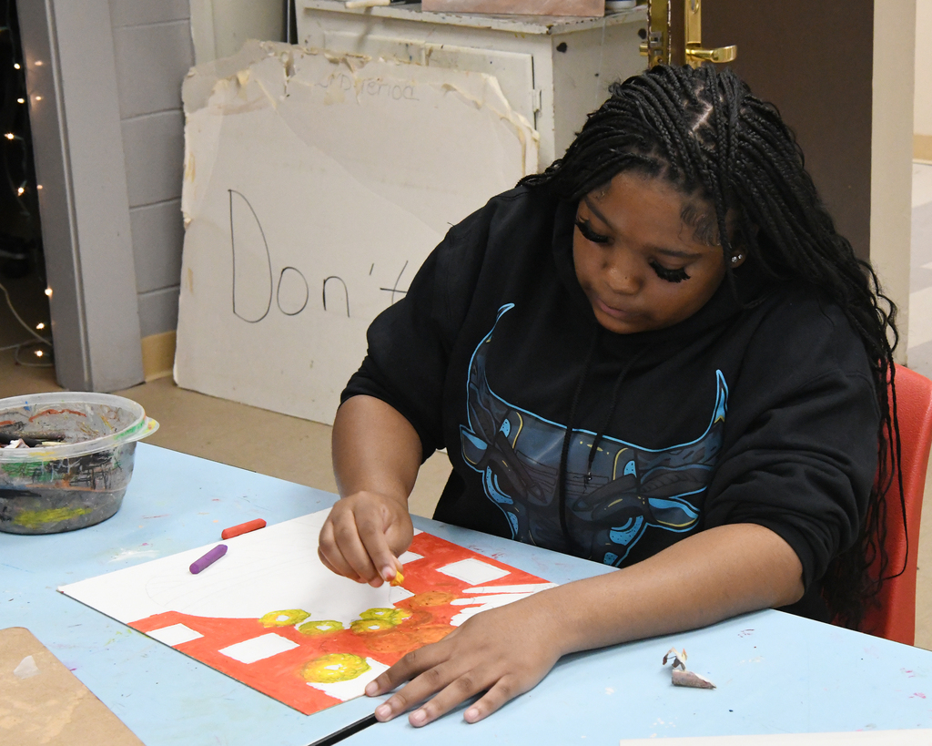 A person wearing a black hoodie sits at a table, coloring a red and yellow design.