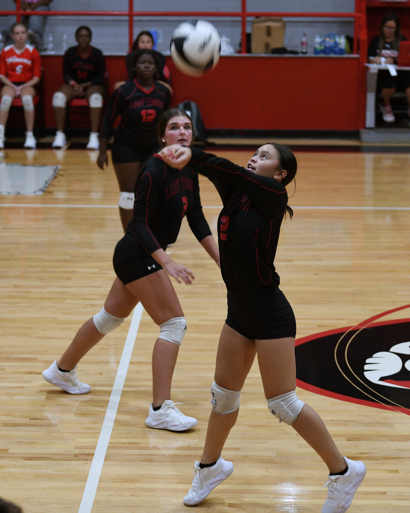 Two women in black jerseys playing volleyball with one attempting to block the ball.