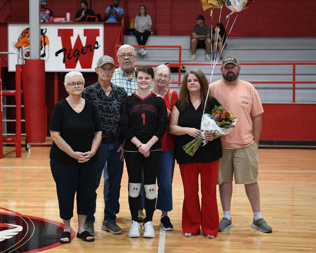 Six adults and a girl in a sports uniform pose for a picture on a basketball court.