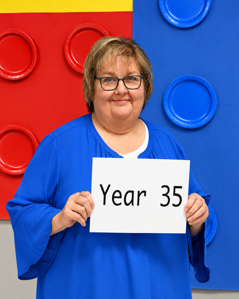 Woman in blue holding a sign saying "Year 35" in front of a backdrop with colorful Lego blocks.