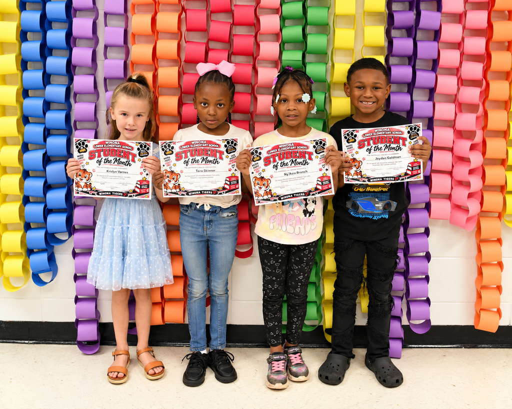 Four children stand in front of a colorful paper chain wall, each holding a certificate.