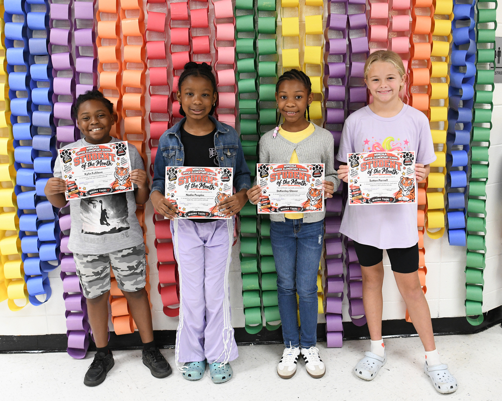 Four children, holding certificates, standing in front of a colorful background.