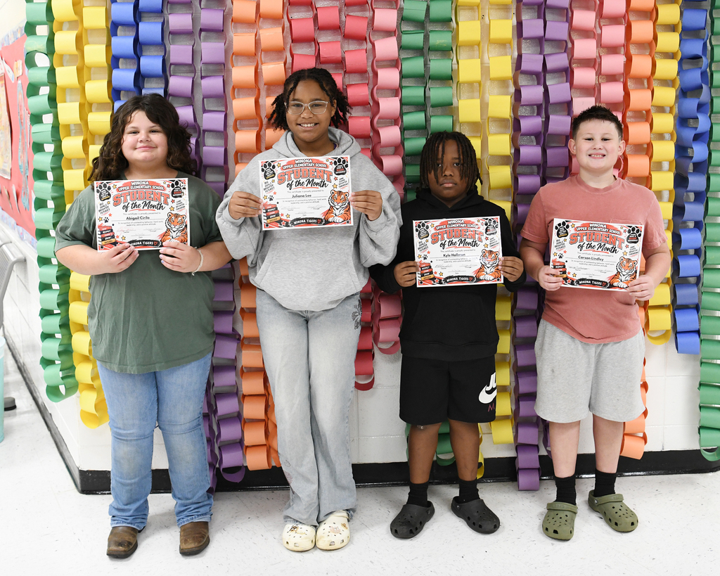 Four students stand together, holding certificates, in front of a colorful, multicolored wall.