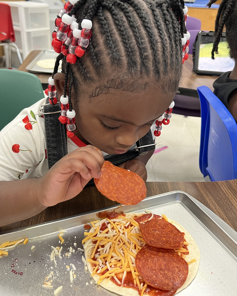 Child with braided hair using a knife to add pepperoni to a homemade pizza with cheese.