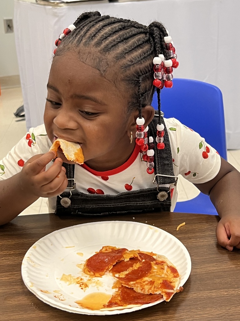 A child with braided hair eats pizza from a paper plate on a brown table.
