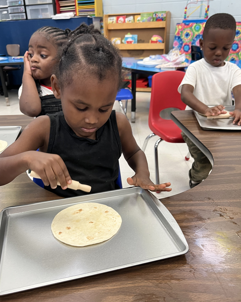 Girl wearing black top uses a wooden stick to spread ingredients on a tortilla on a baking tray.