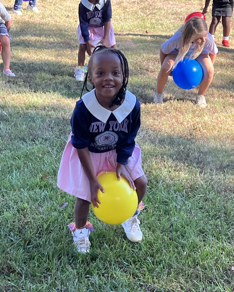 A girl in a pink dress and white shoes holds a yellow balloon while others play with blue balloons.