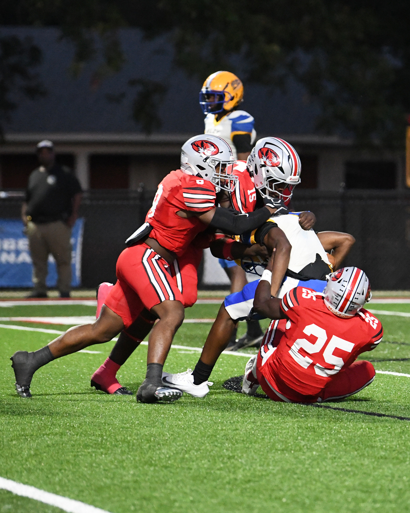 Players on a football field engage in a tackle. Two players are on the ground while others stand nearby.