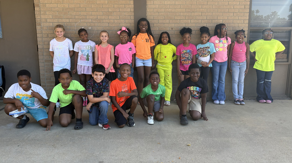 A group of children, some crouching and others standing, in bright-colored shirts, pose for a photo.