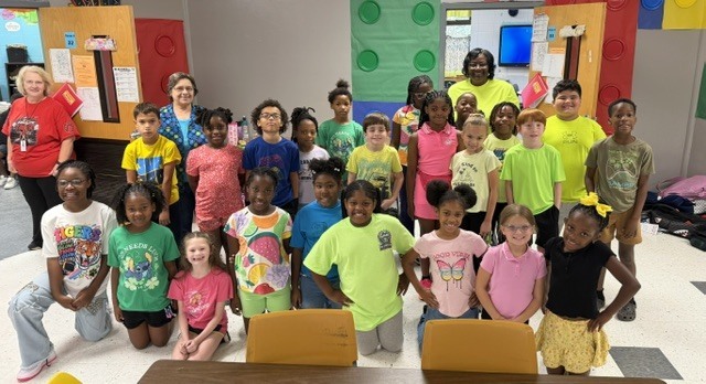 A group of children in colorful shirts, some kneeling and some standing, posing in a room.