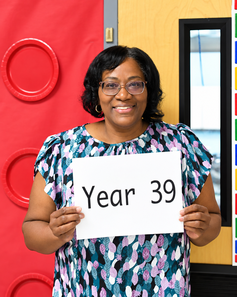 Person wearing glasses holds a white sign with black text "Year 39" in a room.