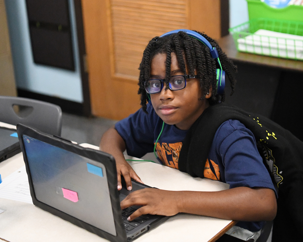 Person with headphones, wearing a blue shirt, sitting at a table with a laptop.
