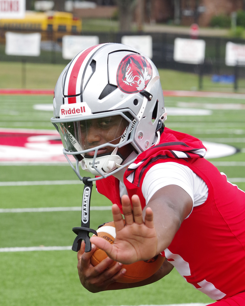 A football player with a helmet holding a ball runs on a field with white lines.