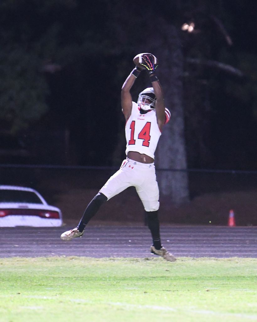 Player in red and white uniform with number 14 catches football mid-air on a football field.