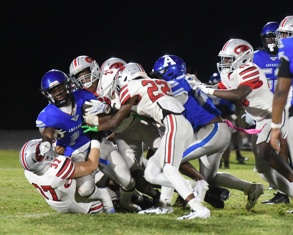 Football players in blue and white uniforms tackle a player in red, white, and blue on a field.