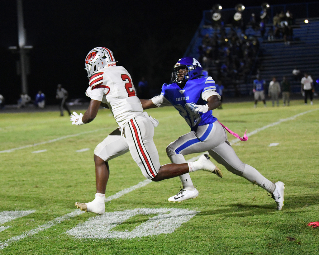 Two football players in action on a field at night. One player in a white uniform, the other in blue.