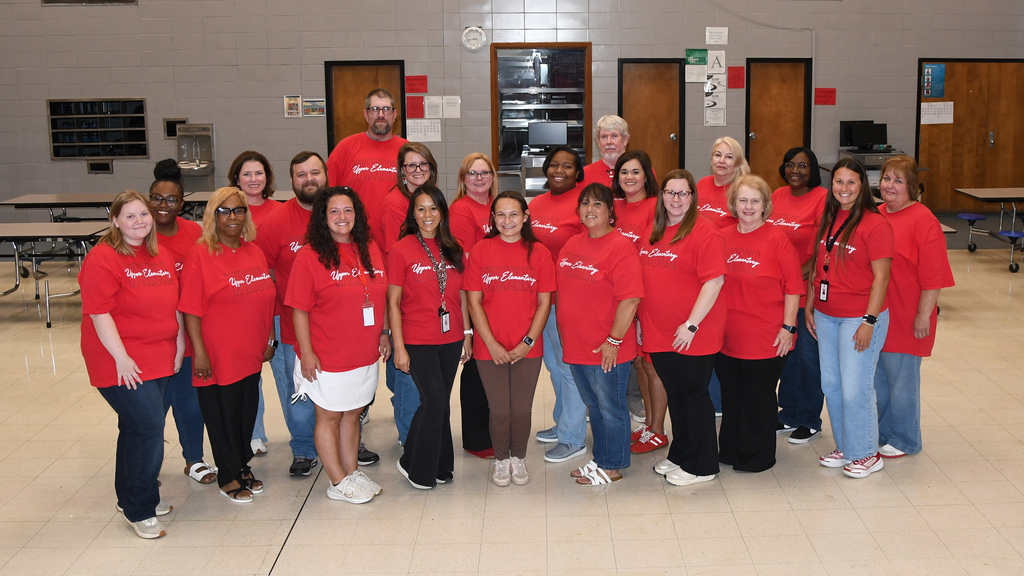 A group of people in red t-shirts stand together in a room with tiled flooring.